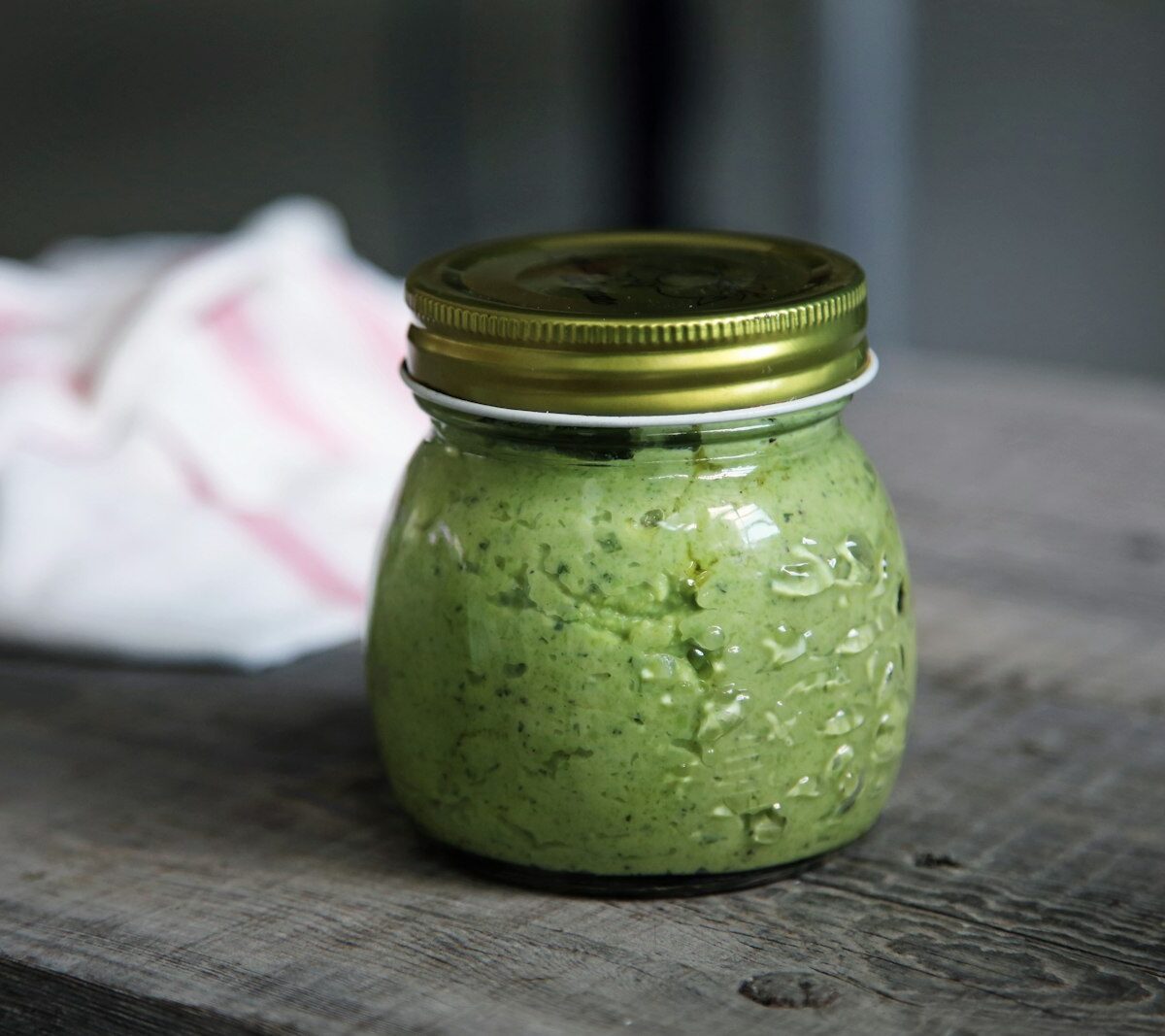 Classic basil pesto spooned into a glass jar, garnished with basil leaves