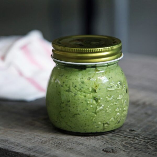 Classic basil pesto spooned into a glass jar, garnished with basil leaves