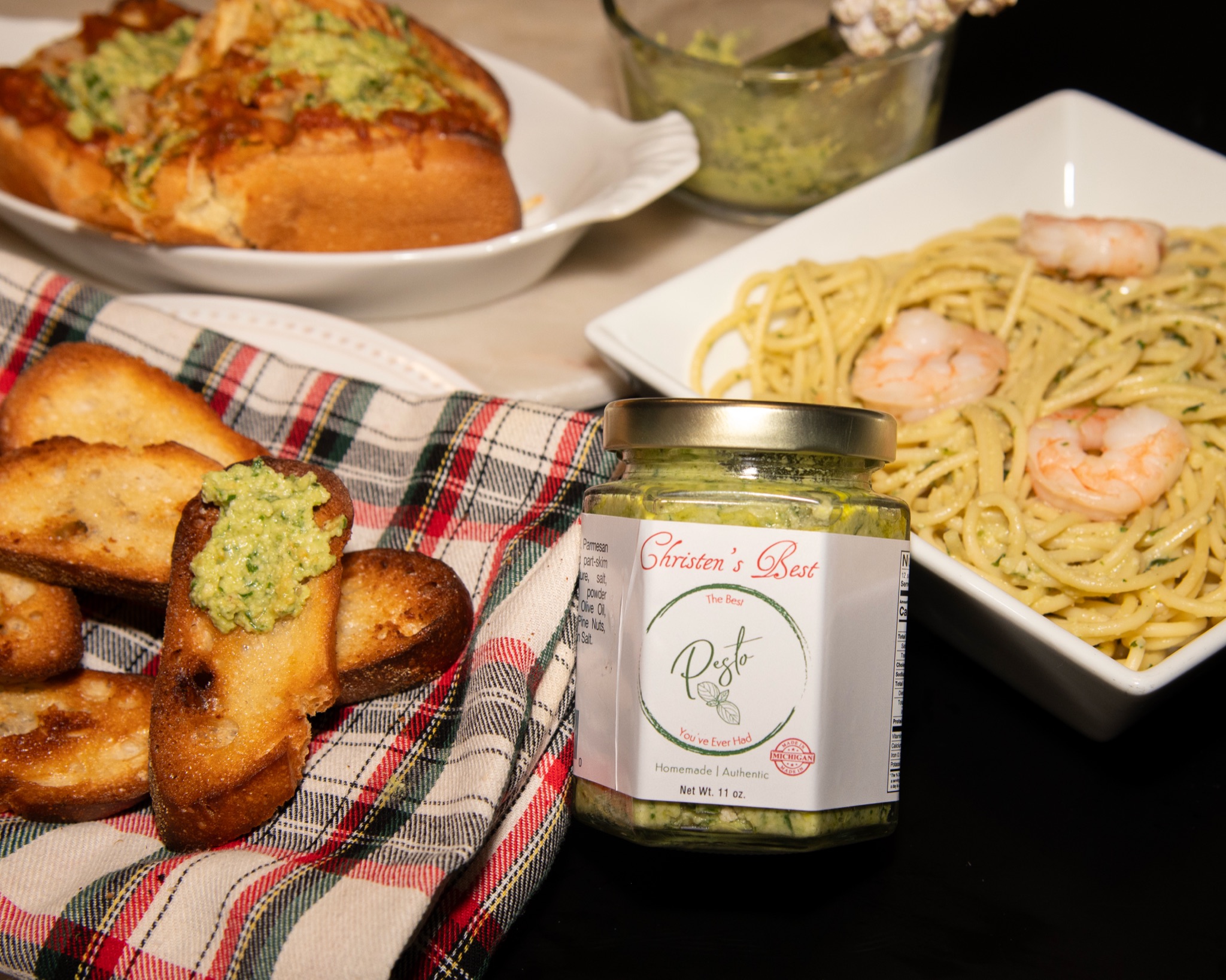 A table set with pesto crostini, shrimp spaghetti, a toasted sub and a jar of Christen's Best pesto